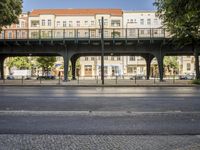 a paved road passing underneath an overpass with cars parked below it on the other side