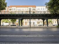 a paved road passing underneath an overpass with cars parked below it on the other side