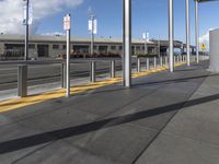 a public area with parking spaces and cars at it, a train station with several metal posts