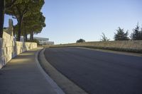 the roadway that runs along a stone wall by a sidewalk with traffic on it and two trees