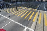 an aerial shot of people walking on the street at an intersection with yellow markings and lines