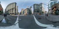 the wide picture shows an intersection in front of tall buildings and cars driving along it