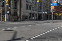 two people wait at an urban intersection on an empty street, as traffic is slowly moving