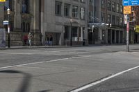 two people wait at an urban intersection on an empty street, as traffic is slowly moving