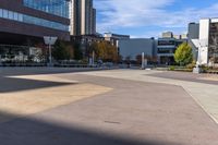 a skateboarder rides down an empty sidewalk in front of a large building with trees