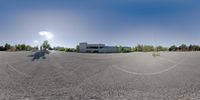 a fish eye photo of an empty parking lot near a building and a small motorcycle parked at one end