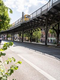 street under the bridge with several people walking on it's sides as well as trees