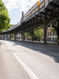 street under the bridge with several people walking on it's sides as well as trees