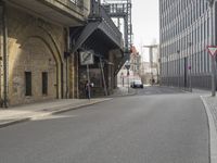 an older, empty street in a town near tall buildings and buildings, some with clock faces, and traffic signs