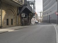 an older, empty street in a town near tall buildings and buildings, some with clock faces, and traffic signs