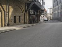 an older, empty street in a town near tall buildings and buildings, some with clock faces, and traffic signs