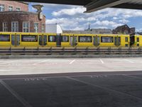 yellow and silver train at train station with graffiti in background and buildings and blue sky