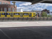 yellow and silver train at train station with graffiti in background and buildings and blue sky