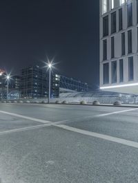 the empty city road is empty by the tall building in the background at night with light streaking on the buildings