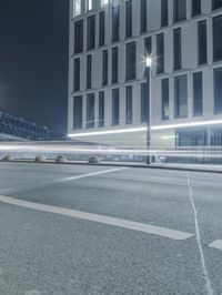 the empty city road is empty by the tall building in the background at night with light streaking on the buildings