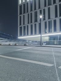 the empty city road is empty by the tall building in the background at night with light streaking on the buildings