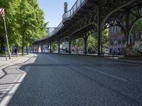trees line the street in front of buildings with lots of windows and many vehicles parked under the bridge