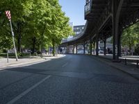 trees line the street in front of buildings with lots of windows and many vehicles parked under the bridge
