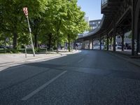 trees line the street in front of buildings with lots of windows and many vehicles parked under the bridge