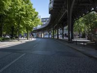 trees line the street in front of buildings with lots of windows and many vehicles parked under the bridge