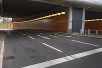 an empty parking lot next to a metal railing and building on a highway, with orange lights above the cars