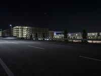 a empty street with cars driving by at night on it and a building in the background