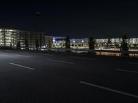 a empty street with cars driving by at night on it and a building in the background