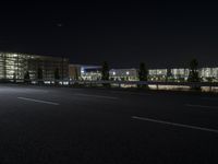 a empty street with cars driving by at night on it and a building in the background