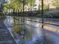 there is a puddle of water on the street next to the road and buildings in the background