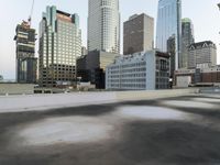 an empty parking lot in the middle of city buildings and a bench with a back wall