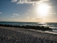 the sun rising over the beach on a sunny day with a small amount of sand