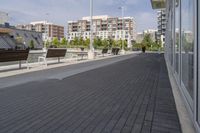 the street has two empty benches along side of it and apartment buildings in the background