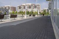 the street has two empty benches along side of it and apartment buildings in the background