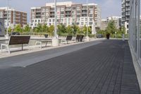 the street has two empty benches along side of it and apartment buildings in the background