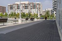 the street has two empty benches along side of it and apartment buildings in the background