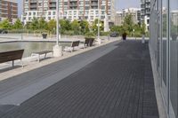 the street has two empty benches along side of it and apartment buildings in the background