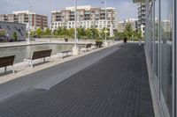 the street has two empty benches along side of it and apartment buildings in the background