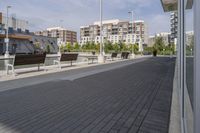 the street has two empty benches along side of it and apartment buildings in the background