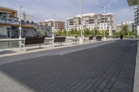 the street has two empty benches along side of it and apartment buildings in the background