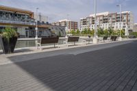 the street has two empty benches along side of it and apartment buildings in the background