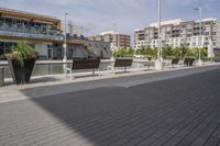 the street has two empty benches along side of it and apartment buildings in the background