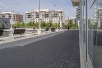 the street has two empty benches along side of it and apartment buildings in the background