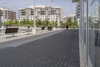 the street has two empty benches along side of it and apartment buildings in the background