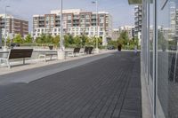 the street has two empty benches along side of it and apartment buildings in the background