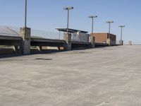 an empty parking lot with multiple street lamps over the road to the left and above it is a man walking toward some parking bays