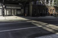 the empty sidewalk has a bus stop at it's side and the shadows come on the pavement