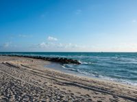 a long stretch of sandy beach covered with sand and water beneath a blue sky with clouds