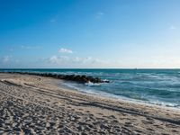 a long stretch of sandy beach covered with sand and water beneath a blue sky with clouds