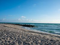 a long stretch of sandy beach covered with sand and water beneath a blue sky with clouds