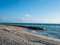 a long stretch of sandy beach covered with sand and water beneath a blue sky with clouds